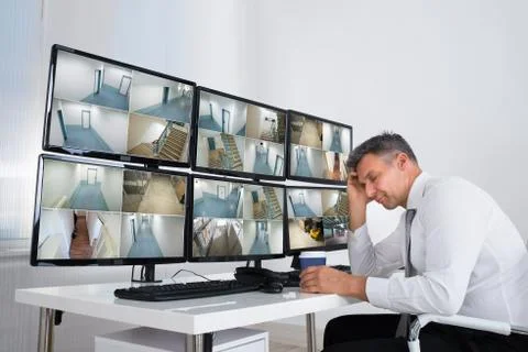 Mature operator sleeping while leaning on security monitor's desk in office Foto stock
