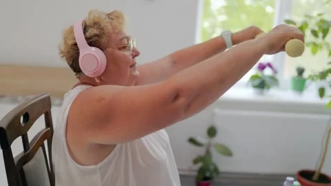 Mature plus size female practicing arm exercises with weights at home fitness at 库存影片 337909196