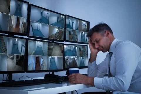 Mature security system operator sleeping while leaning on desk in office Foto stock