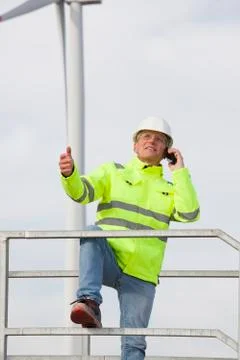 Mature smiling engineer talking on mobile phone in front of a wind turbine Фото