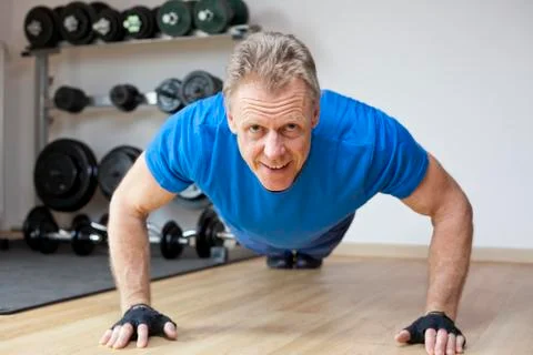 Mature smiling man doing push-ups in a gym - focus on the face Stock Photos