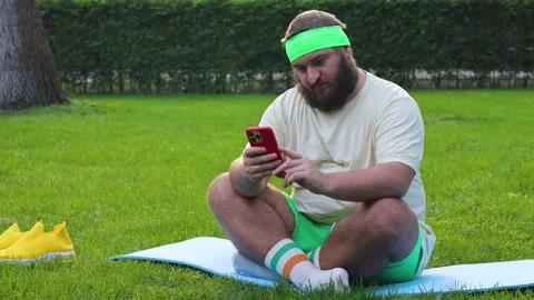 Mature white fat man with beard, green shorts sits on blue yoga mat Stock-Footage 337832181