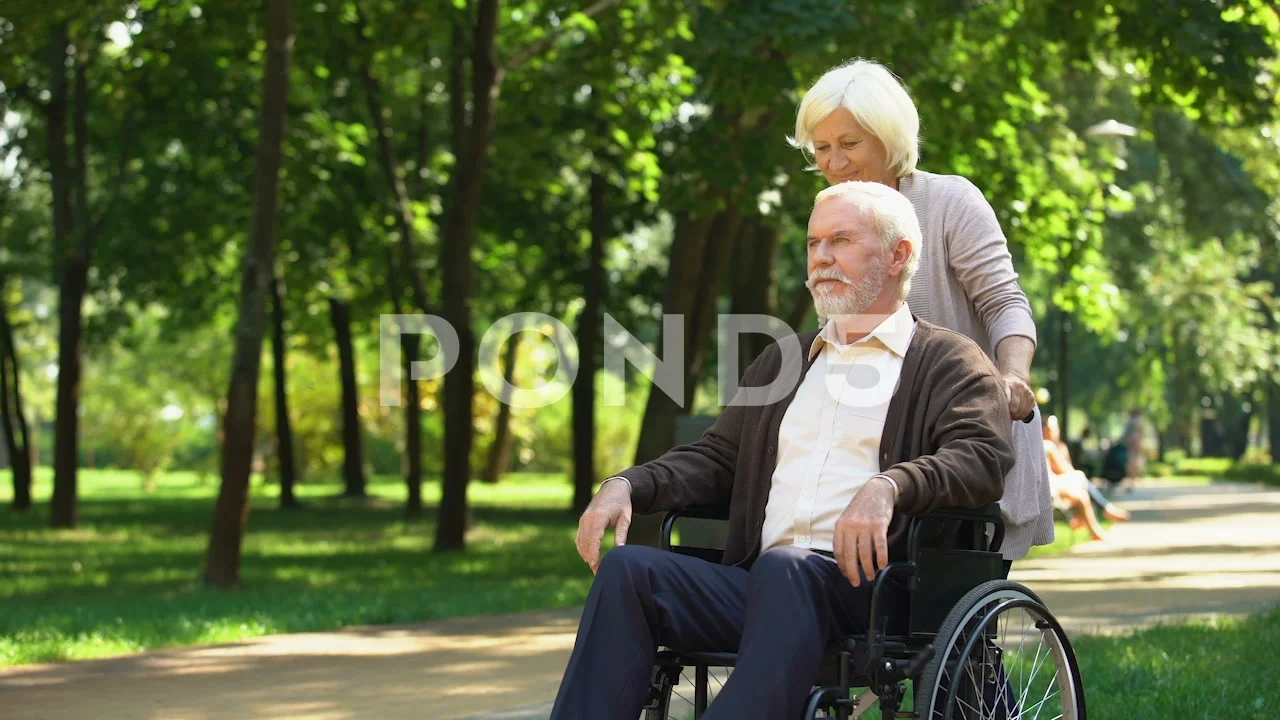 Mature wife taking care of her beloved husband in wheelchair, happy marriage