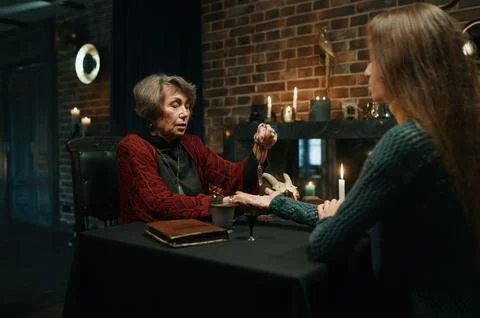 Mature witch using crystal pendulum to predict future for client Fotos Stock