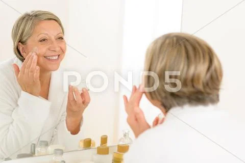 Mature woman apply cream looking bathroom mirror Stock Photos