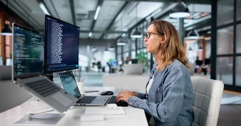 Mature Woman Coding Software On Laptop Using Cloud-based Online Terminal. Stock Photos