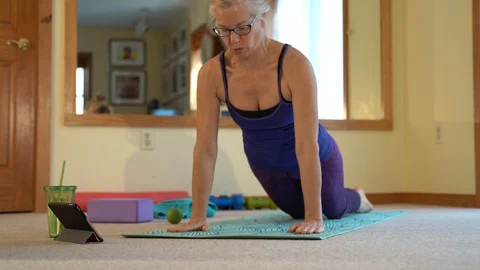 Mature woman doing pushups while watching an online exercise video in a bright Stock Footage 128638645