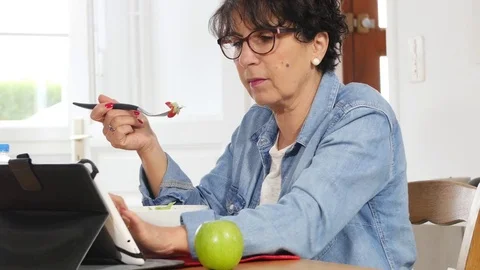 Mature woman looking digital tablet while eating a salad Stock Footage