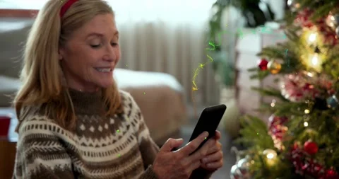 Mature woman picking card while tapping phone, donning antlers, fixing tree Stock Footage 321781886