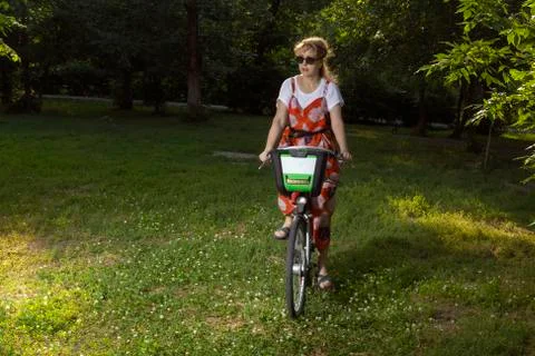 Mature woman rides a bicycle in the evening park. Secluded walk Stock Photos