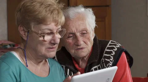 Mature woman with spectacles explaining how to use a tablet to her old haunt 库存影片 59644599