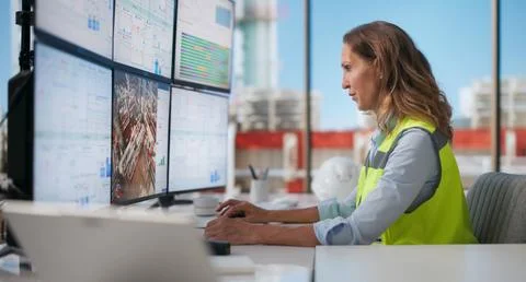 Mature Woman Uses Multiple Computer Screens To Monitor Industrial Plant. 库存照片