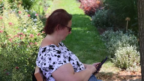 Mature woman using a tablet computer in a sunny park Vídeo Stock 346948998
