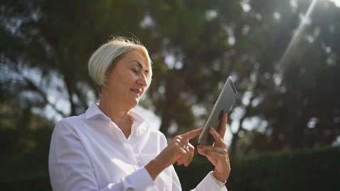 Mature woman using tablet pc while resting at the park Stock Footage 100648378