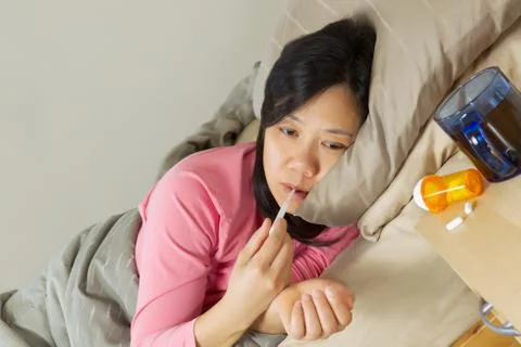 Mature woman using thermometer while lying in bed sick Stock Photos