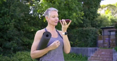 Mature woman using voice command in sportswear with mat queuing yoga session on Stock Footage 339161409