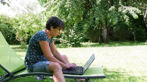Mature woman working at home in the garden on her laptop Stock Footage