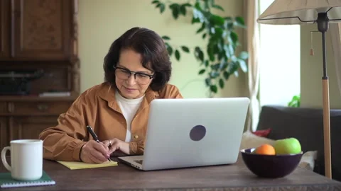 Mature woman write note in notepad and get distant education lesson at home Stock Footage 153898032