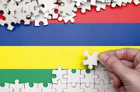 Mauritius flag  is depicted on a table on which the human hand folds a puzzle Foto stock