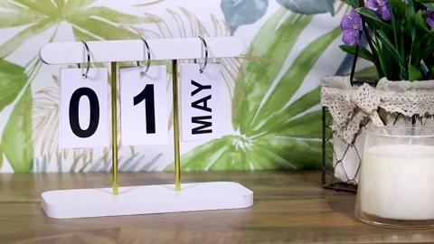 May 1st calendar with candle and flowers near tropical wall on desktop Stock Footage 332114594