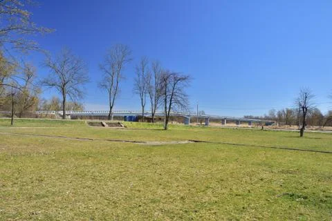 Meadow, lawn and trees on a cloudless day, with a bridge in the background. Stock Photos