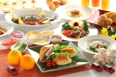Meal table with bacon, orange, beef, fried fish, juice, sanwiches and vegetab Stock Photos