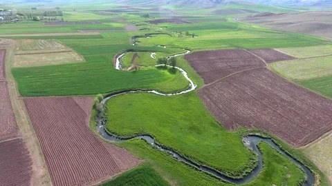 Meandering river winds through patchwork farmland, shaping green and brown Stock Footage 333773002