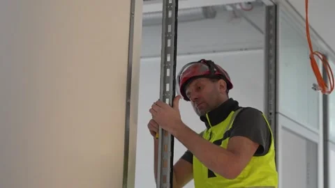 Measuring and aligning metal stud frame for drywall partition, worker preparing Stock Footage 332584352