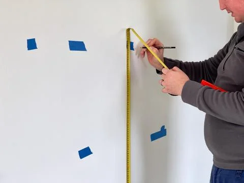 Measuring and marking height on a wall with a yellow tape measure Stock Photos