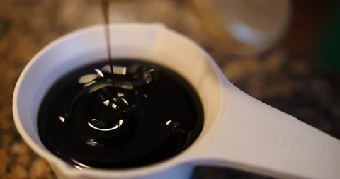 Measuring cup being filled was molasses or gingerbread cook Stock Footage 217355964