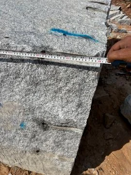 Measuring a granite block in a granite quarry with help of a measuring tape Stock Photos