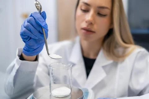 Measuring precise quantities of white powder using a stainless steel spoon in Fotos Stock