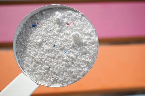 A measuring scoop filled with white laundry detergent powder containing small Stock Photos