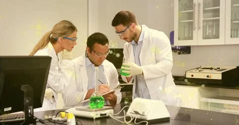 Measuring solutions and recording data at lab bench, chemists in lab coats an Stock Photos