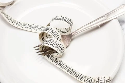 A measuring tape and a fork on a white plate on a marble background Stock Photos