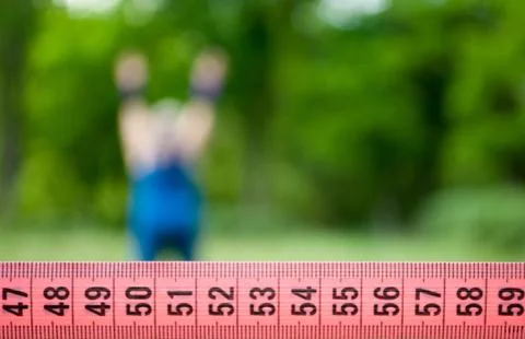 Measuring tape close-up, on background a fat girl is warming up Stock Photos