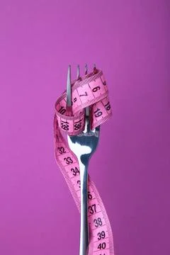 Measuring tape wrapped around fork on pink background. Diet concept Stock Photos
