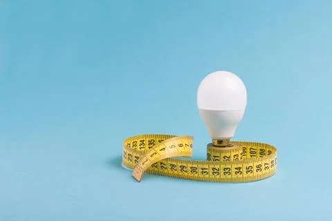 Measuring tape wrapped around a light bulb on a blue background. Minimum crea Stock Photos