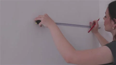 Measuring the wall surface with a tape measure. A young woman renovating a room. Stock Footage 333705354