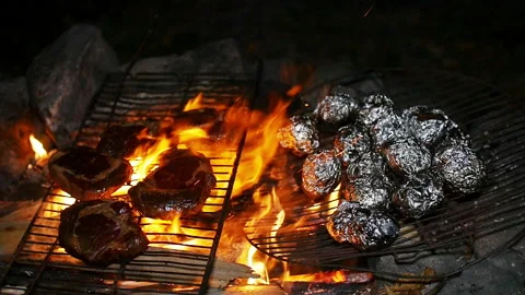 Meat and foil wrapped vegetables grilling over a barbecue fire Stock Footage 153521062