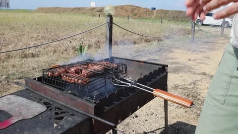 Meat being cooked on a barbecue grill over an open fire in a field Stock Footage 313656534