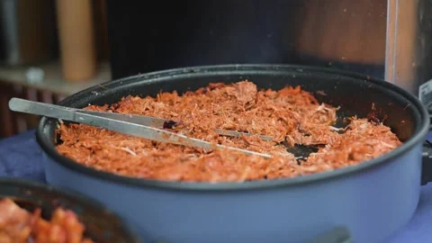 Meat is being cooked in a large pan at an outdoor event. The setting includes Stock Footage 345885720