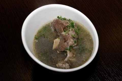 Meat in the broth with some herbs served in the white bowl Stock Photos