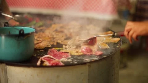 Meat cooks on hot griddle beside steaming pot during community celebration Stock Footage 345346725