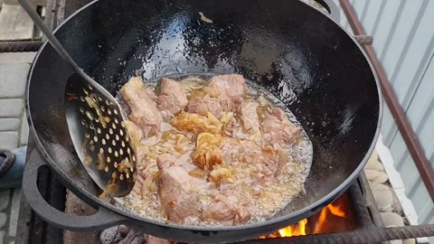 Meat is fried in a cauldron over an open fire. pilaf preparation process Stock Footage 152633181