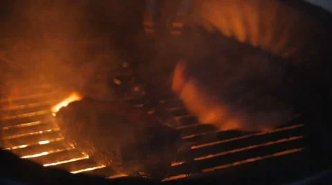 A meat on a gas grill with open flames is cooked with a metal spatula Video stock 67354000