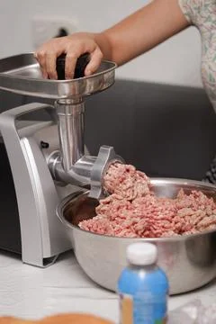 Meat grinding process in a kitchen with a metal grinder and fresh ground meat Stock Photos