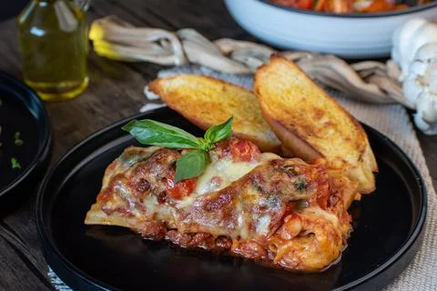 Meat lasagna with basil and bread in an elegant black plate Stock Photos