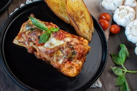 Meat lasagna with basil and bread in an elegant black plate top view Foto stock