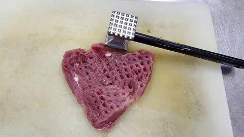 Meat Mallet Tenderizing Raw Beef Steak on a White Cutting Board in Kitchen Stock-Fotos